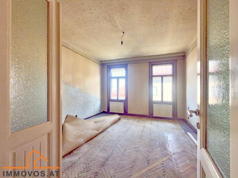 Geräumiger Raum mit Fischgrätparkett, hohen Decken und großen Fenstern, bereit zur Renovierung.