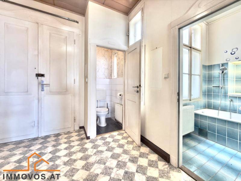 Flur mit Schachbrettmuster-Fliesenboden und Zugang zu WC und Badezimmer.