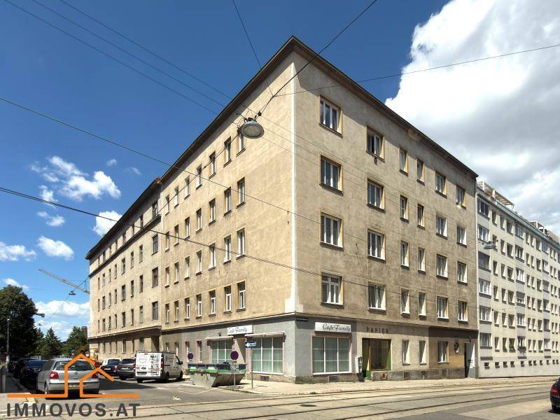 Eckgebäude mit mehreren Etagen und Geschäften im Erdgeschoss an einer städtischen Straße.