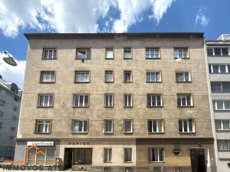 Fassade eines Mehrfamilienhauses mit vielen Fenstern und einem Geschäft im Erdgeschoss.