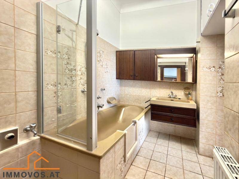 Badezimmer mit Badewanne, Duschabtrennung und Waschbecken, ausgestattet mit hellen Fliesen.