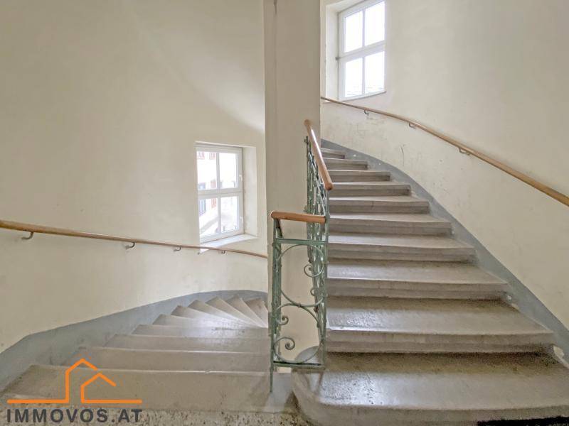 Historisches Treppenhaus mit Steinstufen, schmiedeeisernem Geländer und Fenstern für natürliches Licht.