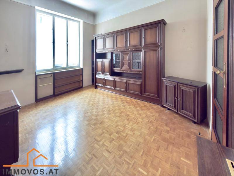 Geräumiges Zimmer mit traditionellem Holzschrank und Parkettboden, gut beleuchtet durch ein großes Fenster.