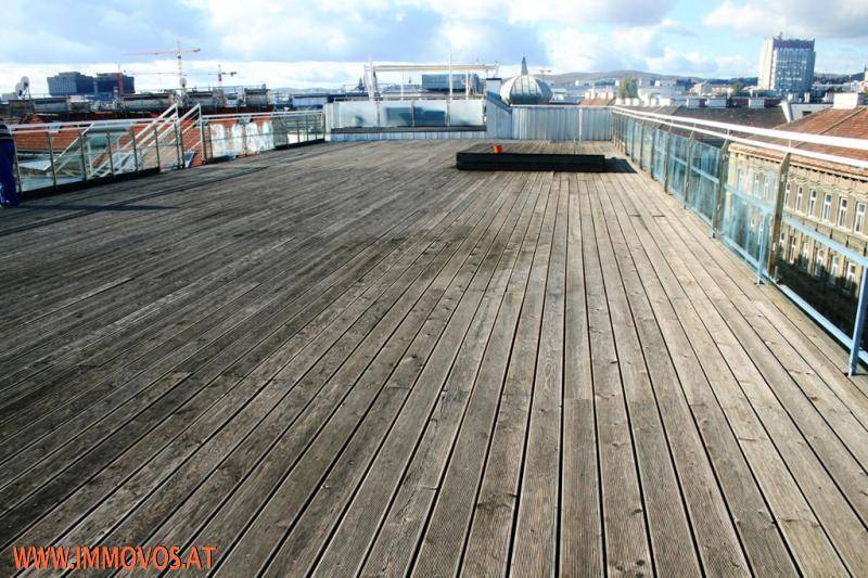 Weitläufige Dachterrasse mit Holzboden und Panoramablick über die Stadt und den Himmel.