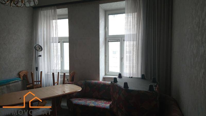 Wohnzimmer mit Sofa, Esstisch und Stühlen, beleuchtet durch zwei Fenster.