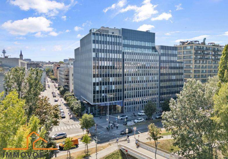 Großes modernes Bürogebäude in städtischer Umgebung mit viel Grün und belebter Straße.