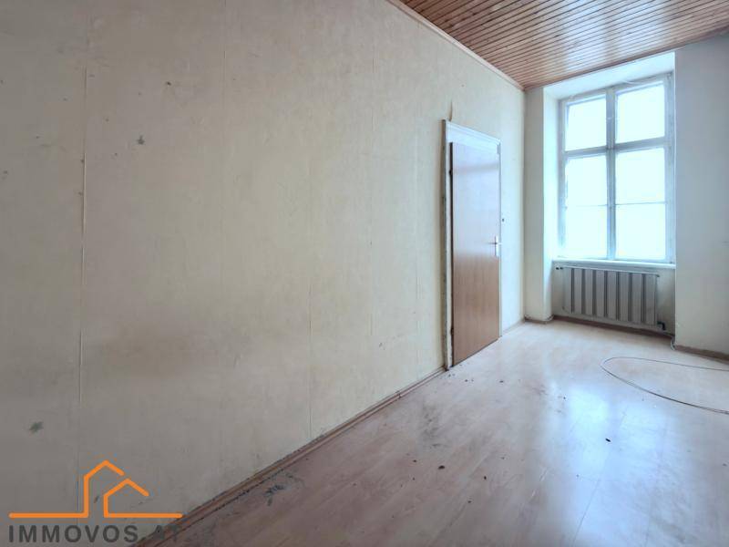 Unrenovierter Raum mit Holzboden, einer Tür und einem großen Fenster, das viel Licht hereinlässt.