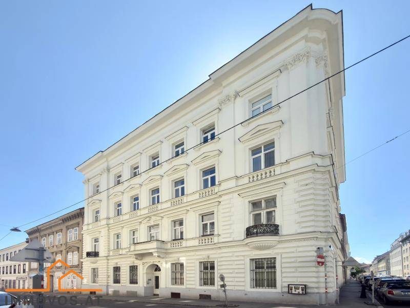 Elegantes weißes Altbaugebäude mit vielen Fenstern und dekorativen Balkonen unter blauem Himmel.