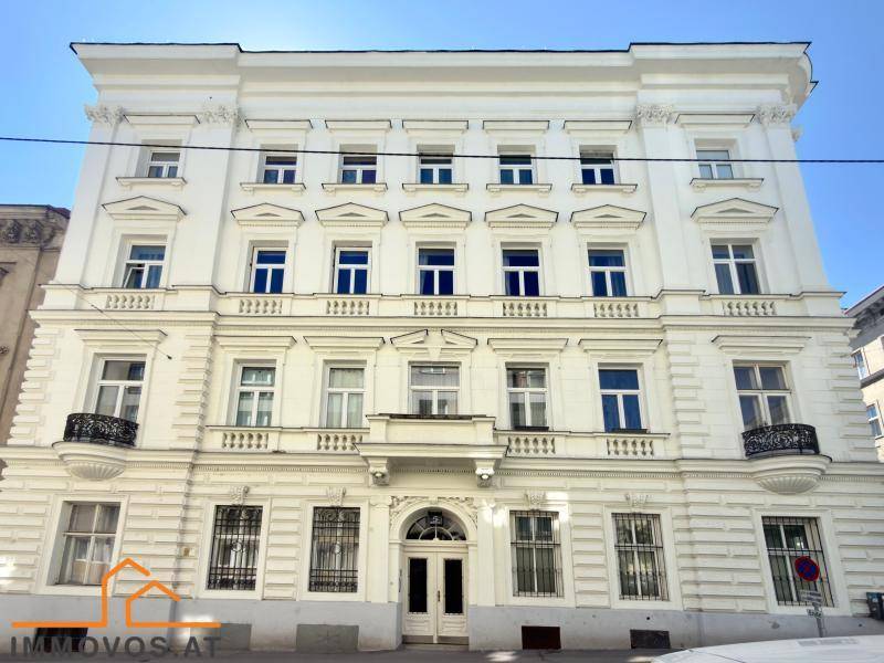Prächtige weiße Fassade eines Altbaus mit symmetrischen Fenstern und verzierten Balkonen.