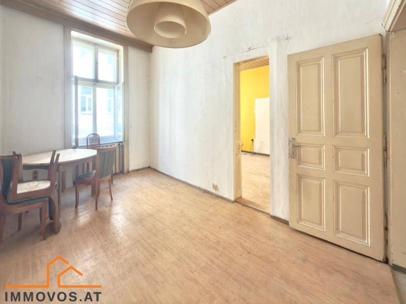 Helles Zimmer mit Holzboden, Holztisch und Stühlen, bereit für eine Renovierung.