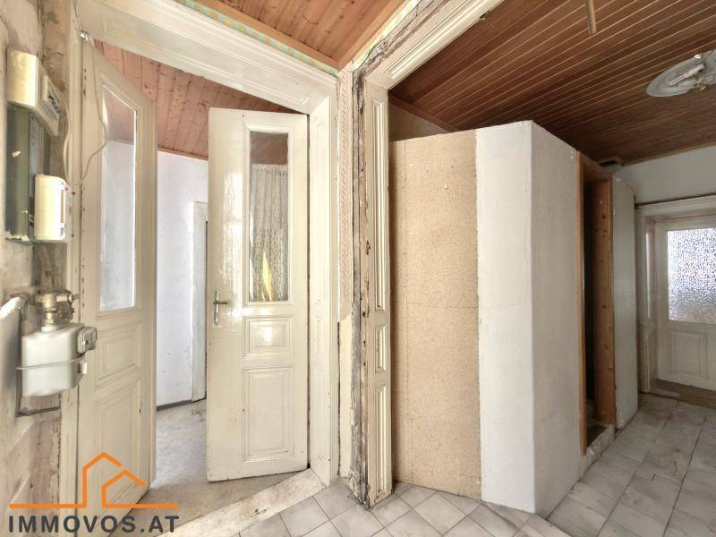 Flur mit Holztäfelung an der Decke, Fliesenboden und mehreren Türen, die zu anderen Räumen führen.