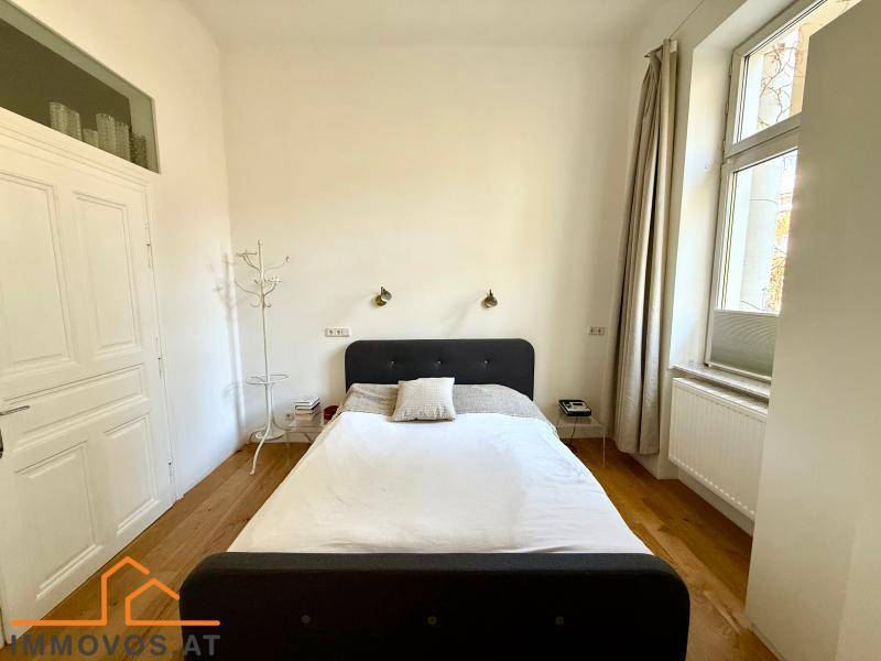 Helles Schlafzimmer mit Holzboden, großem Fenster und schlichtem Doppelbett.