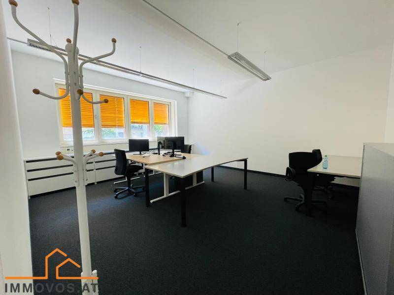 Heller Büroraum mit mehreren Arbeitsplätzen, Teppichboden und Jalousien an den Fenstern.