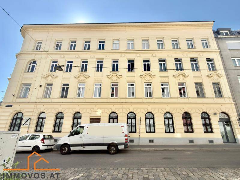 Klassische Altbaufassade eines Mehrfamilienhauses an einer städtischen Straße mit parkenden Fahrzeugen.