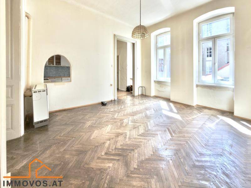 Lichtdurchflutetes Zimmer mit Fischgrätparkett, Wandheizung und großen Fenstern, die viel Tageslicht hereinlassen.
