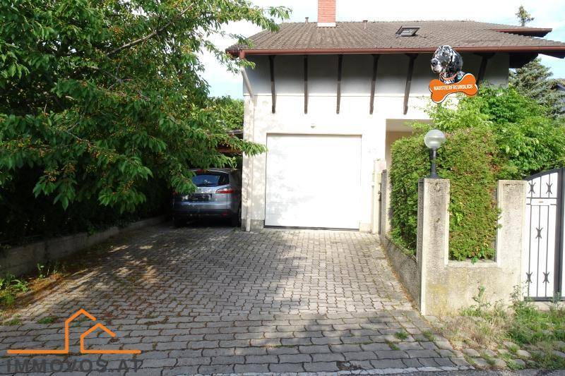 Einfahrt mit gepflastertem Weg und integrierter Garage, umgeben von grünen Hecken.