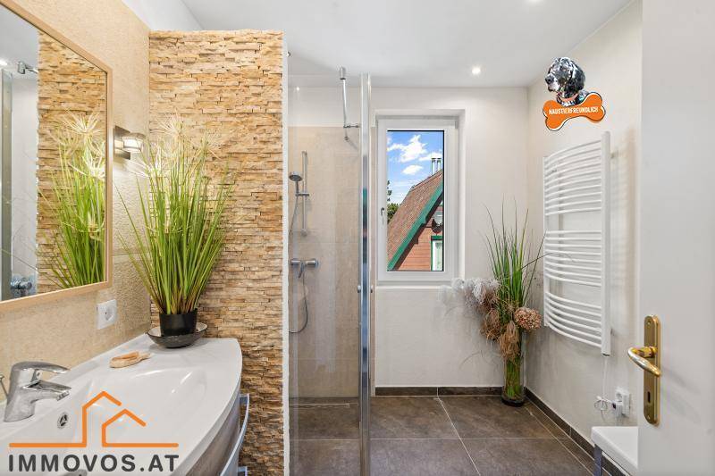 Modernisiertes Badezimmer mit begehbarer Dusche, Steinwandakzent und beheiztem Handtuchhalter.