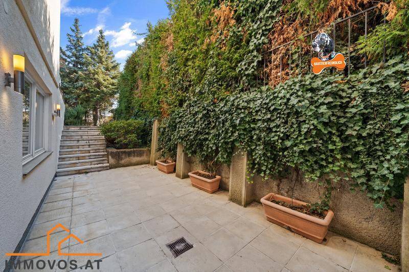 Gepflasterte Terrasse mit Treppenzugang zum Garten, umgeben von üppigem Grün.