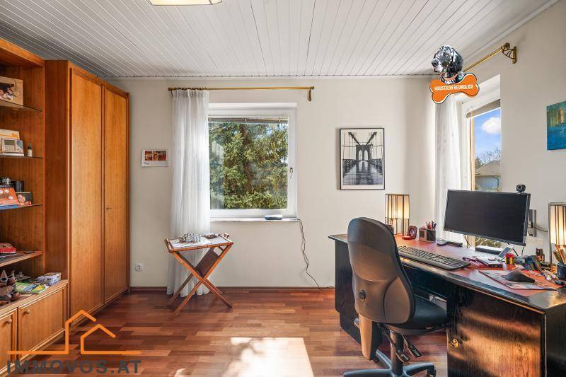 Helles Arbeitszimmer mit Holzboden, großem Schreibtisch und Blick ins Grüne durch das Fenster.
