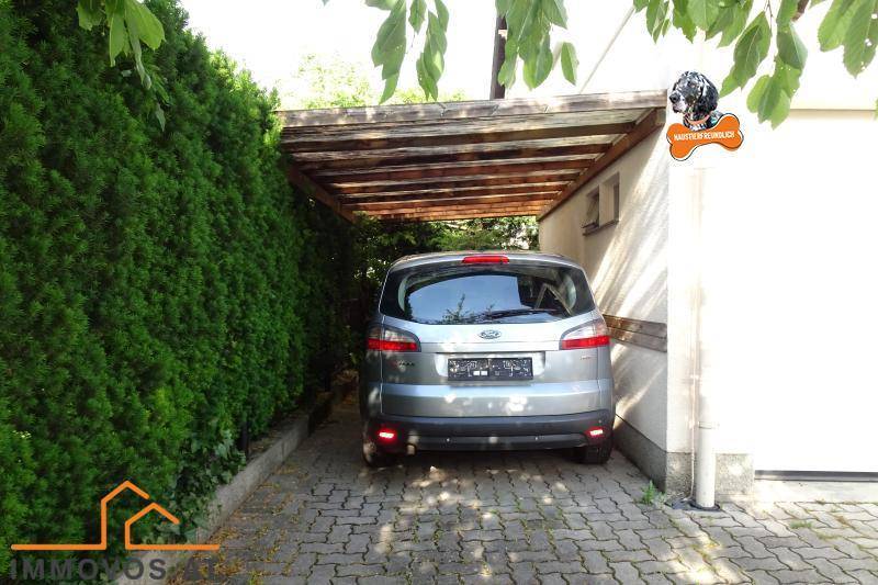 Überdachter Stellplatz (Carport) neben dem Haus, umgeben von einer hohen Hecke.
