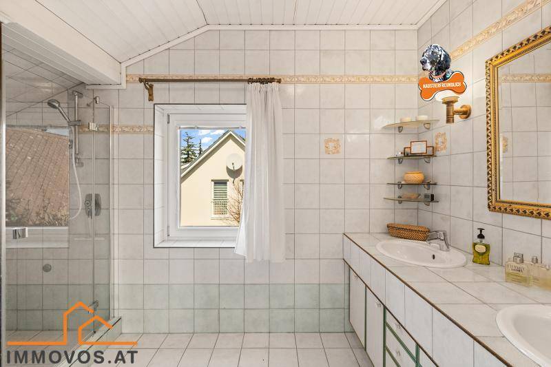 Gefliestes Badezimmer mit Badewanne, Duschbereich und Fenster mit Blick ins Grüne.