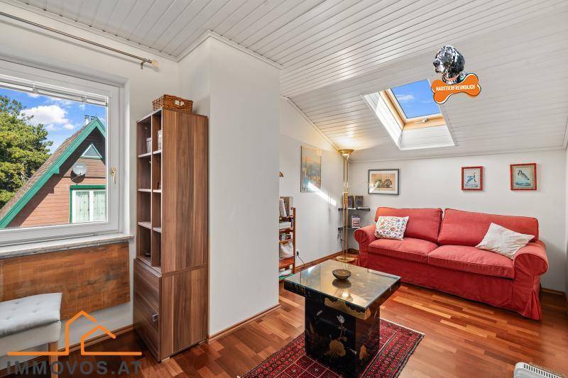 Gemütlicher Wohnbereich mit Holzboden, rotem Sofa, Dachschräge und Dachfenster für Helligkeit.