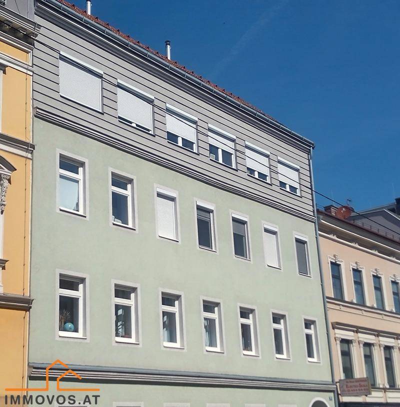 Fassade eines Mehrfamilienhauses mit hellgrüner Putzfassade und Rollläden an den Fenstern.