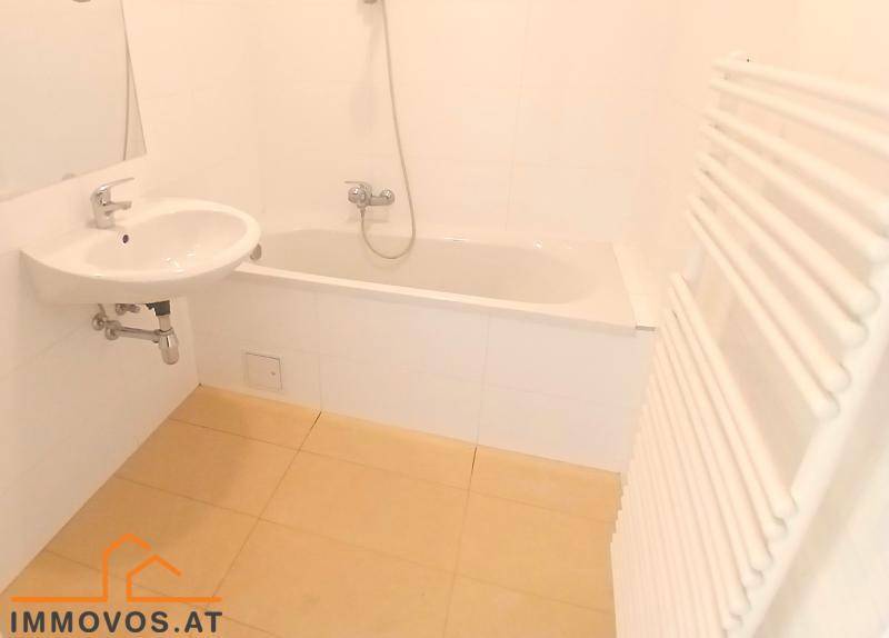 Modernes Badezimmer mit Badewanne, Waschbecken und beheiztem Handtuchhalter, hell gefliest.