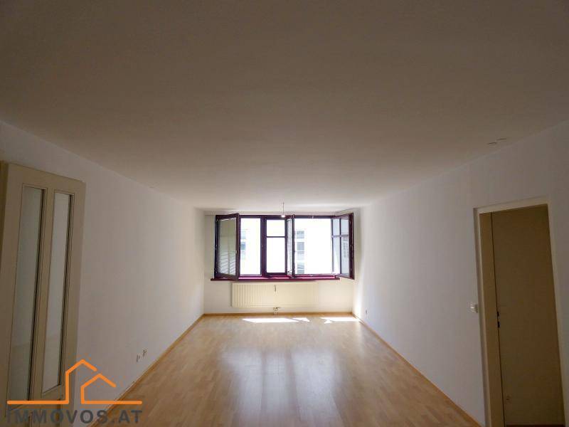 Heller Wohnraum mit Holzboden, weißen Wänden und einem Erkerfenster, das viel Tageslicht hereinlässt.