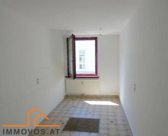 Leerer Raum, möglicherweise eine Küche, mit gemustertem Fliesenboden, weißen Wänden und einem Fenster.