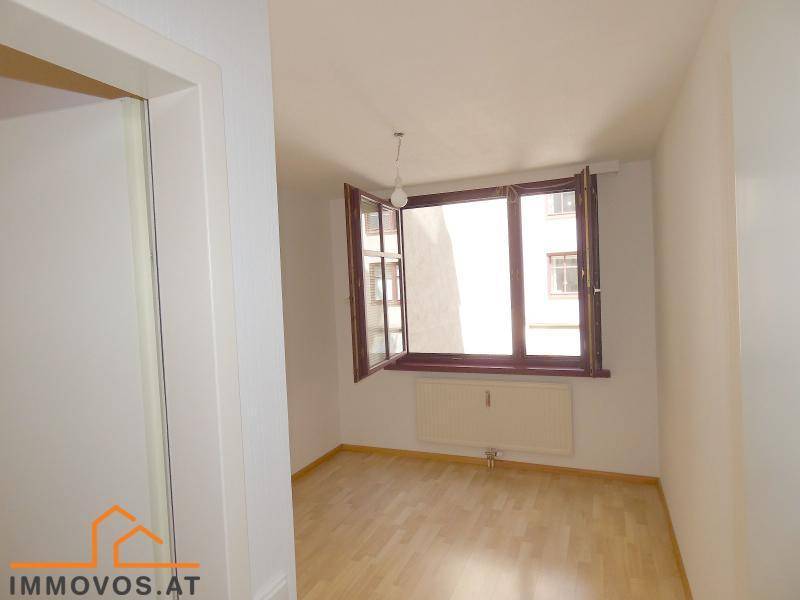 Helles Zimmer mit Holzboden, weißen Wänden und einem Fenster mit Blick nach draußen, das viel Licht spendet.