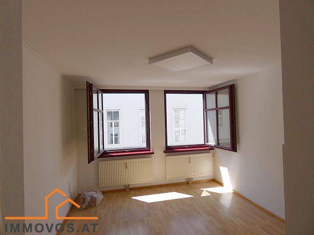 Helles Schlafzimmer mit Holzboden, weißen Wänden und zwei Fenstern, die viel natürliches Licht spenden.
