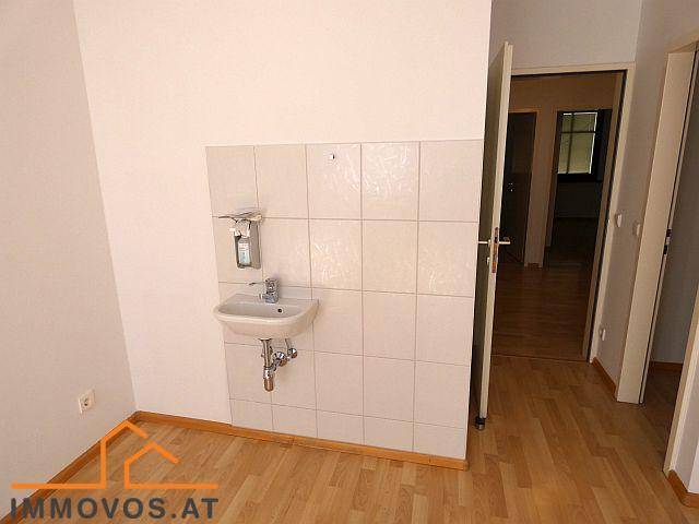 Raum mit hellem Holzboden und einem gefliesten Bereich an der Wand mit einem kleinen Waschbecken.