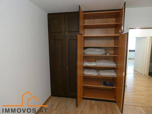 Zimmer mit hellem Holzboden und einem großen, offenen Kleiderschrank aus dunklem Holz mit vielen Fächern.