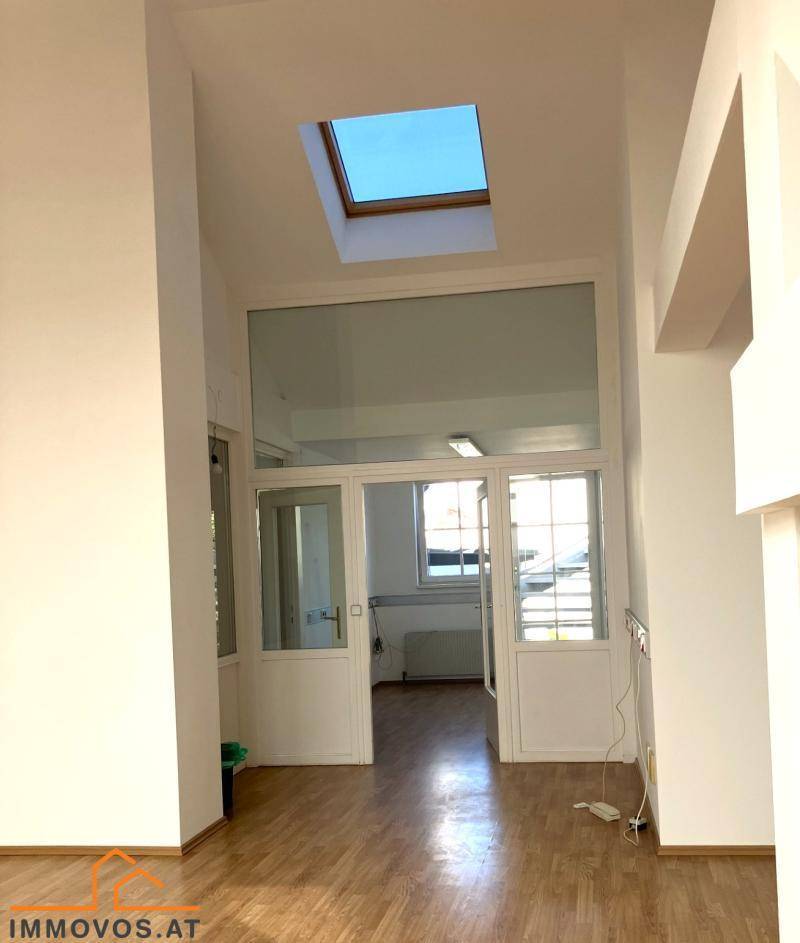 Heller Raum mit Holzboden, einem Dachfenster und Glastüren, die zu einem weiteren Bereich führen.