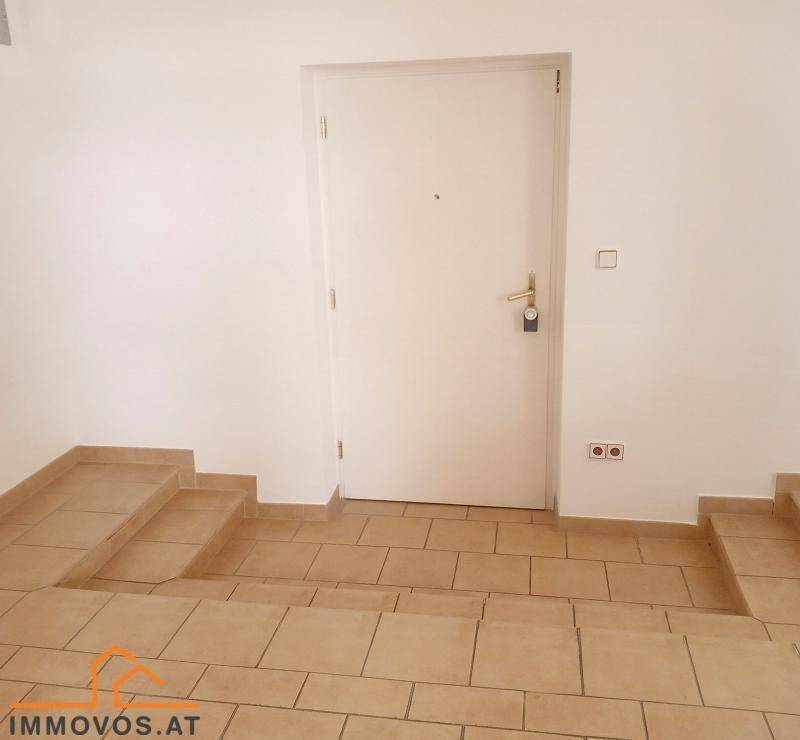 Eingangsbereich mit gefliestem Boden, Stufen und einer weißen Eingangstür, die in die Wohnung führt.