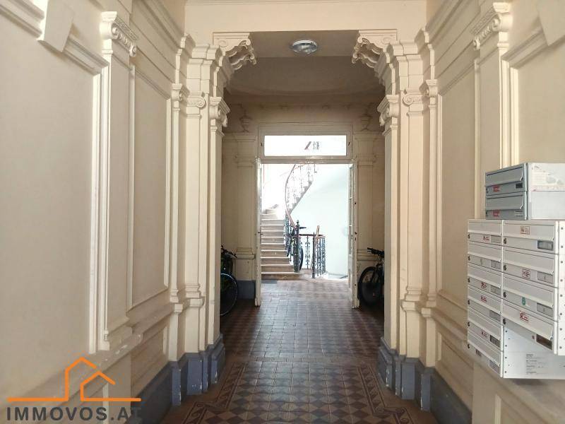 Historischer Eingangsbereich mit Stuckverzierungen, Fliesenboden und Blick auf eine Wendeltreppe.