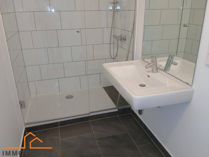 Modernes Badezimmer mit ebenerdiger Dusche, weißem Waschbecken und dunklen Bodenfliesen in minimalistischem Design.