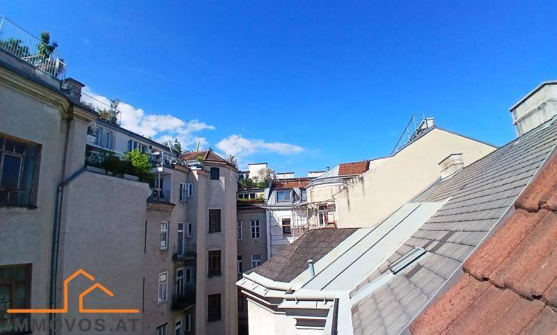 Blick über die Dächer der Stadt mit angrenzenden Gebäuden und begrünten Terrassen unter blauem Himmel.