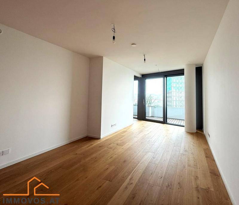 Heller Raum mit Holzboden und großen Fenstern, die Zugang zu einem Balkon bieten und viel Tageslicht hereinlassen.