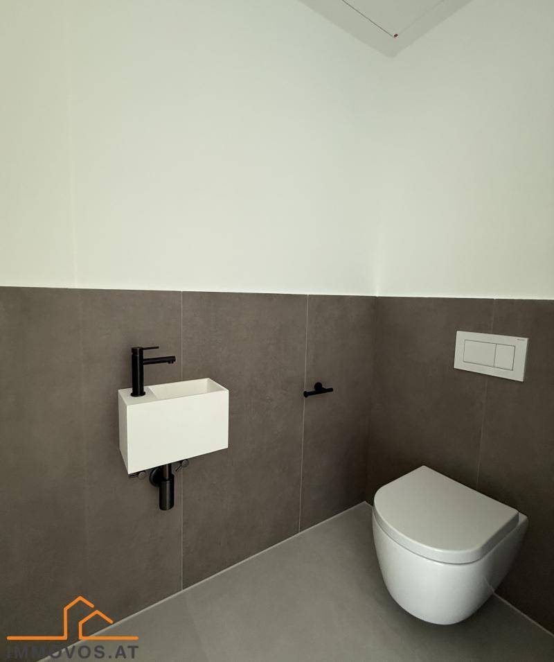 Modernes Gäste-WC mit wandhängender Toilette und kleinem Waschbecken, halbhoch gefliest in Grau.