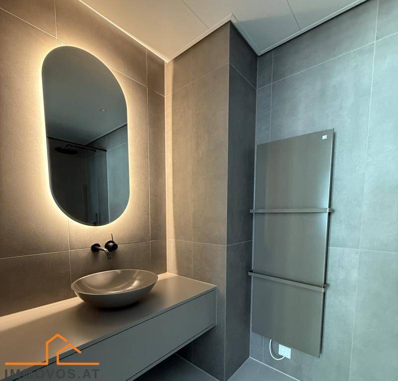 Modernes Badezimmer mit grauen Fliesen, beleuchtetem Spiegel und stilvollem Aufsatzwaschbecken.