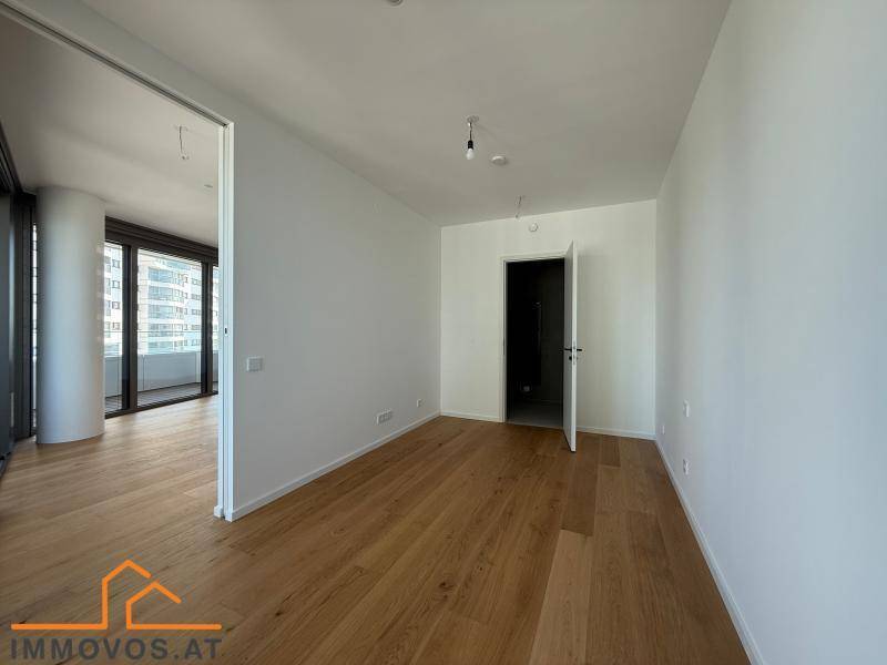 Helles Schlafzimmer mit Holzboden und Zugang zu einem Balkon durch große Fenstertüren.