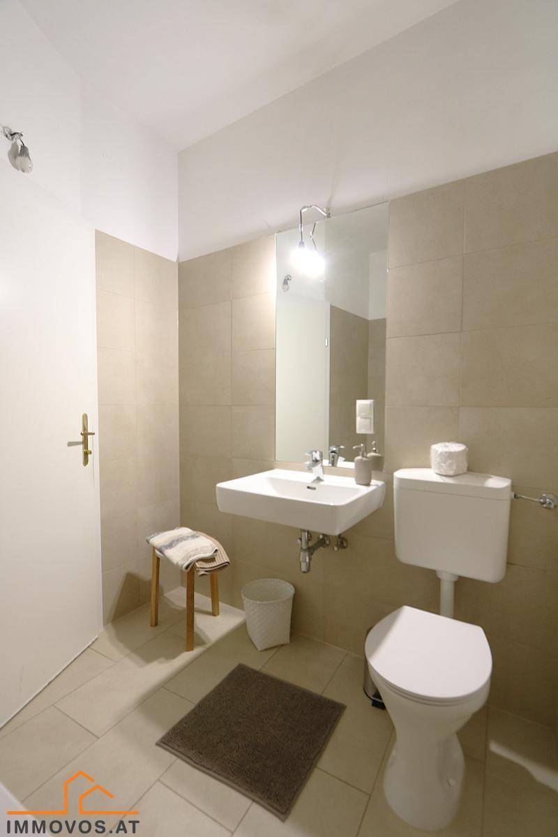 Modernes Badezimmer mit Waschbecken, Toilette und beigefarbenen Fliesen.