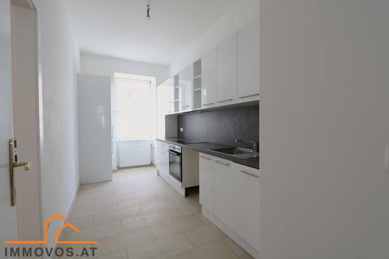 Moderne Küche mit weißen Hochglanzschränken, dunkler Arbeitsplatte und Fenster.