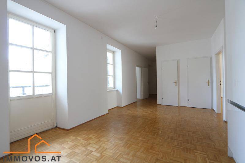 Heller, leerer Raum mit Fischgrätparkettboden und Zugang zu einem Balkon.