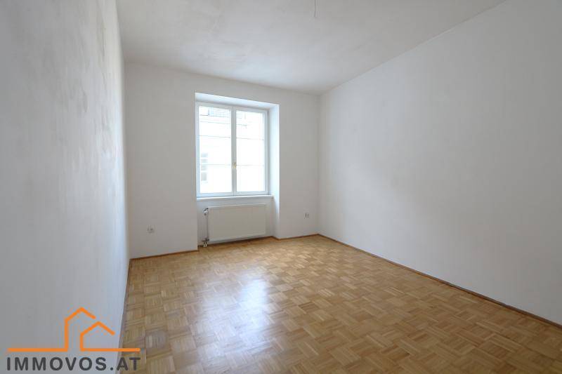 Heller, leerer Raum mit Fischgrätparkettboden und einem großen Fenster.