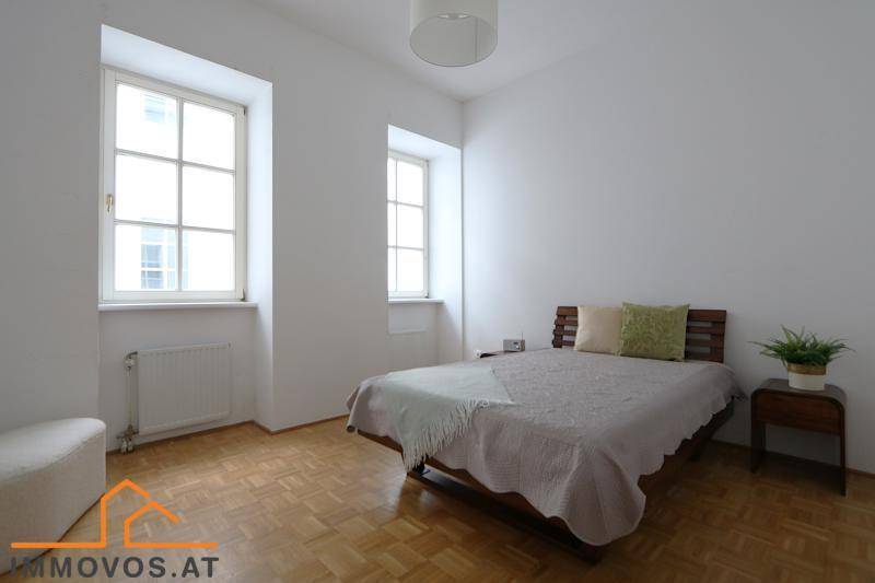 Gemütliches Schlafzimmer mit Holzbett, Nachttisch und Fischgrätparkettboden.