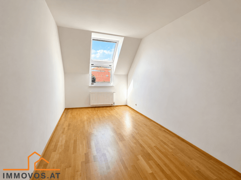 Schlafzimmer mit Holzboden, Dachschräge und einem großen Dachfenster, das viel Licht hereinlässt.