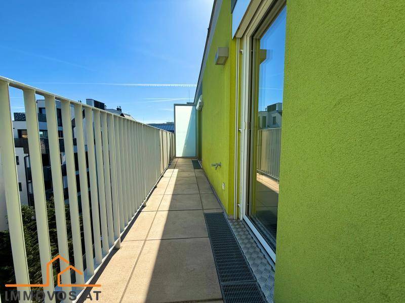 Langer, schmaler Balkon mit grüner Fassade und hellem Geländer unter blauem Himmel.